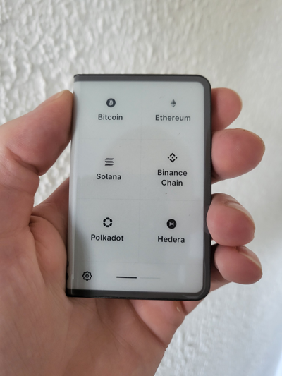 Ledger Stax hardware wallet displaying cryptocurrency wallets for Bitcoin, Ethereum, Solana, Binance Smart Chain, Polkadot, and Hedera on E Ink screen